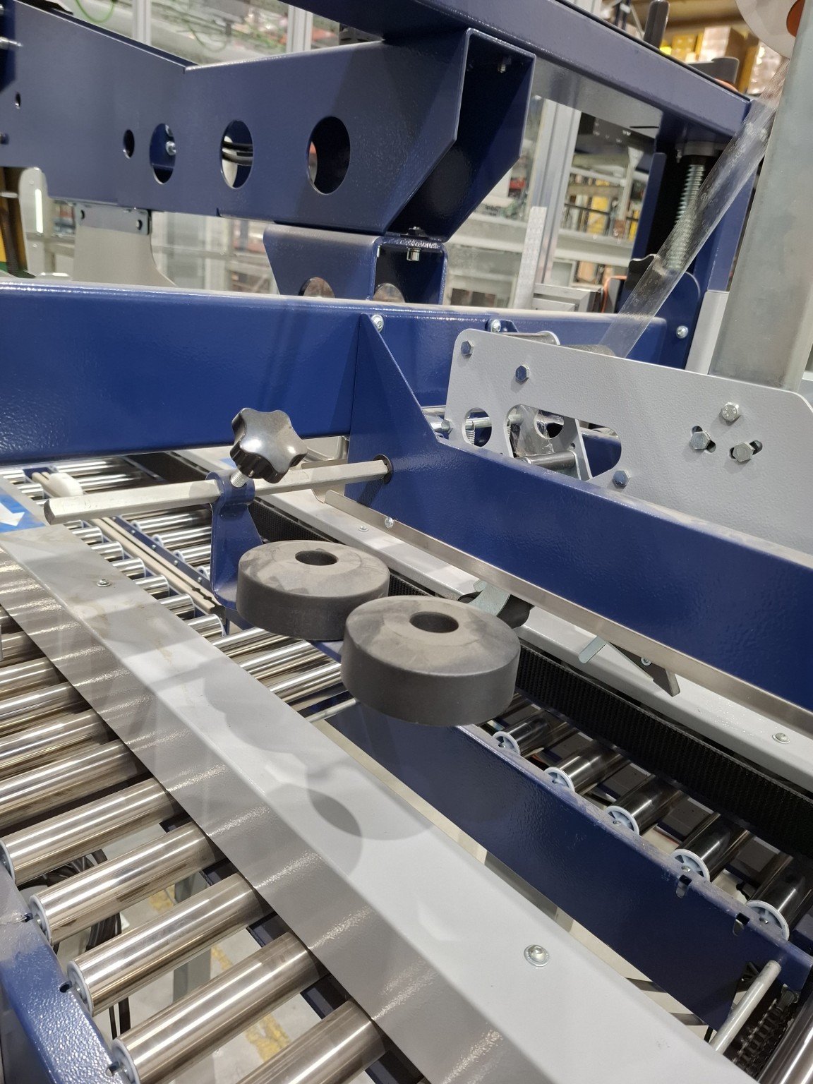 Detalhe de equipamento de embalagem automatizado, com estrutura azul e transportador de roletes
